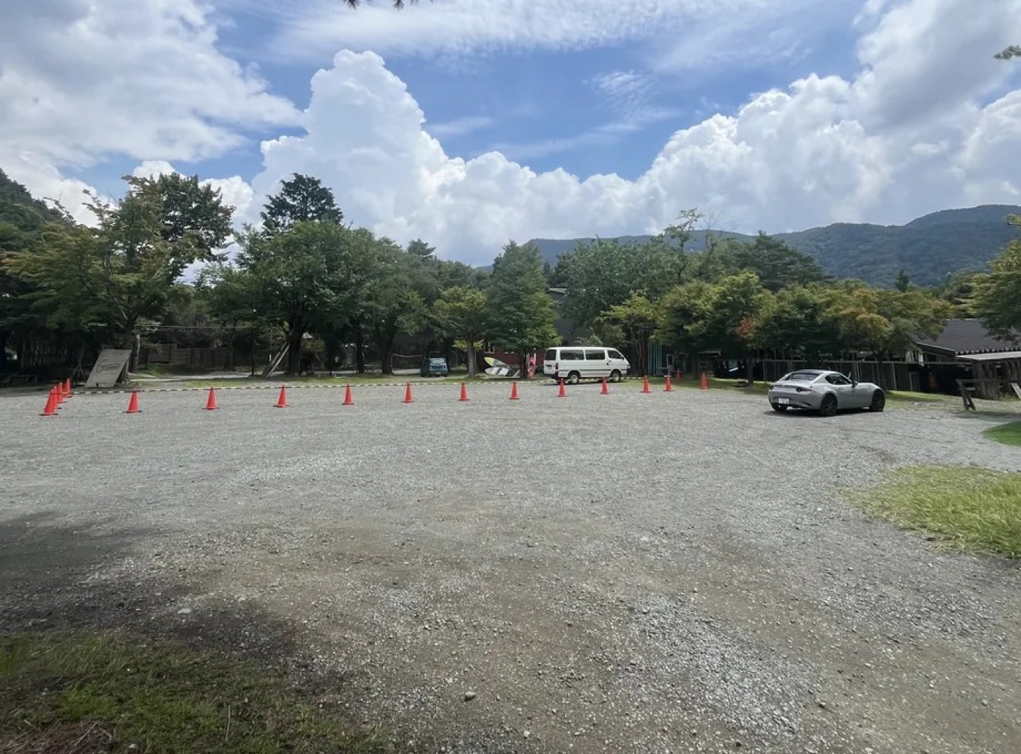 木々と山を背景に、車と赤いコーンが並ぶノームの場内駐車場